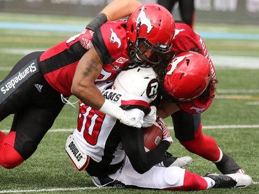 Redblacks receiver Chris Williams is tackled by Stampeders Alex Singleton and Tommie Campbell.