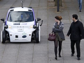 Pedestrians watch as a self-driving vehicle is tested on a road in London, England.