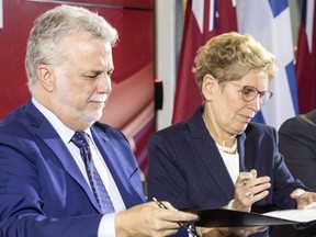 Quebec Premier Philippe Couillard, left, and Ontario Premier Kathleen Wynne pass a document between themselves as they sign an agreement after a joint meeting of cabinet ministers in Toronto on Friday, October 21, 2016.