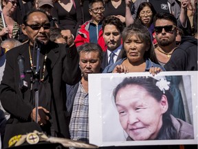 Prime Minister Justin Trudeau listens in the background as Annie Pootoogook's cousin Sytukie Joamie speaks alongside her brother Pauloosie Joanasie  and her cousin Kilatja Simeonie, holding a photo of Pootoogook.