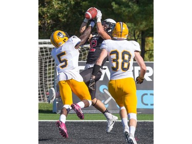 Windsor DB Lekan Idowu (L) tries to block Ravens receiver Kyle Van Wynsberghe as he makes the catch for a touchdown with Devon Woods (R) moving in as the Carleton Ravens take on the Windsor Lancers in OUA football action at MNP Park on the Carleton University campus.
