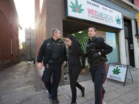 A woman is arrested and placed in a cruiser as Ottawa police conduct raids on a number of pot shops, including WeeMedical on Rideau Street.
