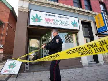 An officer places crime tape at the scene as Ottawa police conduct raids on a number of pot shops including Wee Medical on Rideau St.