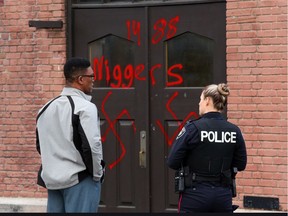 Rev. Anthony Bailey and a police officer inspect racist graffiti at Parkdale United Church Friday. Postmedia has blurred the racist epithet on the door.