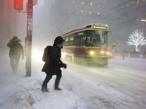 A person struggles through snow to a streetcar as snow flies through the air during a squall in downtown Toronto, on Thursday, December 15, 2016. THE CANADIAN PRESS/Graeme Roy