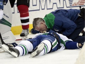 A trainer talks to Vancouver Canucks defenceman Philip Larsen, of Finland, after he was knocked down on a hit by New Jersey Devils left wing Taylor Hall during the second period of an NHL hockey game, Tuesday, Dec. 6, 2016, in Newark, N.J. Larsen left the game on a stretcher.