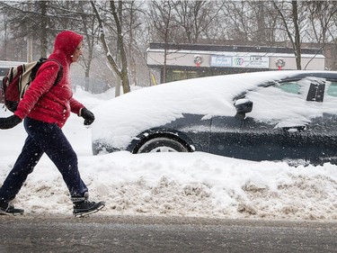 A woman walks past a snow covered car parked on Byron Ave as the region is blanketed with fresh snow overnight.