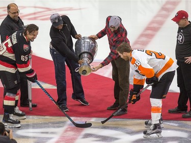 Henry Burris and Brad Sinopoli of the Ottawa Redblacks drop the puck from the Grey Cup for the ceremonial face off as the Ottawa Senators take on the Philadelphia Flyers in NHL action at Canadian Tire Centre. Taking the face-off are Erik Karlsson and Claude Giroux with Marcel Desjardins (L) and Rick Campbell (R) looking on.