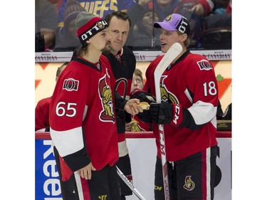 Dion Phaneuf and Ryan Dzingel watch captain Erik Karlsson eat a hot dog.