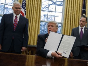 Vice President Mike Pence, left, and White House Chief of Staff Reince Priebus watch as President Donald Trump shows off an executive order to withdraw the U.S. from the 12-nation Trans-Pacific Partnership trade pact agreed to under the Obama administration.