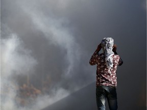 A Palestinian protester watches as smoke rises during clashes with Israeli security forces following a demonstration against the expropriation of Palestinian land by Israel in the village of Kfar Qaddum, near Nablus, in the occupied West Bank on December 30, 2016. /