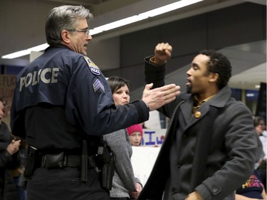 James Badue, who is with the Minnesota NAACP, leads other opponents in a chant: "No hate, no fear, immigrants are welcome here," as an airport police officer tries to quiet him, at the Minneapolis-St. Paul International Airport on Saturday, Jan. 28, 2017, in Minneapolis.