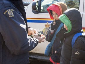 An RCMP officer checks the passports of two young asylum claimants after crossing the border into Canada from the United States, Monday, February 20, 2017 near Hemmingford, Que. A growing number of people have been walking across the border into Canada to claim refugee status.