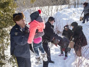 Family members from Somalia are helped into Canada by RCMP officers along the U.S.-Canada border near Hemmingford, Que., on Friday, February 17, 2017. A number of refugee claimants are braving the elements to illicitly enter Canada.