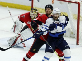 Winnipeg Jets' Bryan Little (18) is checked by Ottawa Senators Marc Methot (3) as Senators goaltender Mike Condon keeps his eye on the flying puck during first period NHL hockey action in Ottawa on Sunday, February 19, 2017.