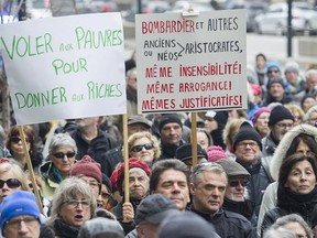 People hold up signs during a demonstration outside Bombardier&#039;s head office in Montreal, Sunday, April 2, 2017, to protest recent pay hikes and bonuses to the company&#039;s top executives. THE CANADIAN PRESS/Graham Hughes