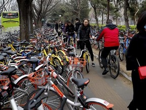 In this Thursday, March 23, 2017 photo, residents ride bicycles from bike-sharing company Ofo try to pedal through a sidewalk crowded with bicycles from the bike-sharing companies Ofo, Mobike and Bluegogo, near a bus stand in Beijing, China. As many as 2.2 million of these two-wheelers have been deployed, which are available for rent for as little as U.S. 7 cents for half an hour, in the latest symbol of heavy spending in China&#039;s internet sector where startups are in a race to attract more users