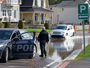 A Gatineau police officer observes a vehicle pushing through the flood water along Rue Jacques-Cartier Tuesday in the old section of Gatineau along the Ottawa River near the Gatineau River.