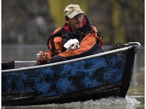 A man holds a dog as they navigate floodwaters by boat on Rue Saint-Louis in Gatineau, Que., as rising river levels and heavy rains continue to cause flooding, on Saturday, May 6, 2017.