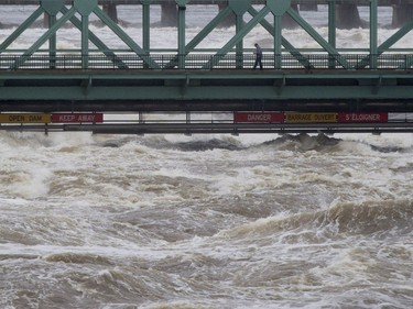 A pedestrian walks across the Chaudiere bridge as high waters on the Ottawa river pass just under Saturday May 6, 2017 in Ottawa.