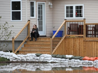 A woman sits on a porch from a flooded house on Morin Road in Cumberland on Monday.