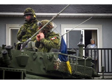 The Canadian Forces were called into Gatineau to help with the flooding in Gatineau Sunday May 7, 2017. CF members make their way along Rue Campeau after filling the light armoured vehicle with sandbags. A woman watches from the doorway of a balcony above.