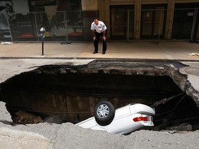 A St. Louis police officer looks over a large hole in 6th Street, Thursday, June 29, 2017, in St. Louis, that swallowed a Toyota Camry between Olive and Locust Streets. It isn&#039;t immediately clear what caused the collapse. (Christian Gooden/St. Louis Post-Dispatch via AP)