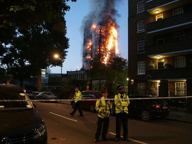Police man a security cordon as a huge fire engulfs the Grenfell Tower early June 14, 2017 in west London.  The massive fire ripped through the 27-storey apartment block in west London in the early hours of Wednesday, trapping residents inside as 200 firefighters battled the blaze. Police and fire services attempted to evacuate the concrete block and said "a number of people are being treated for a range of injuries", including at least two for smoke inhalation.