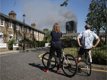 Local residents watch smoke billow from Grenfell Tower, a residential block on June 14, 2017 in west London.  The massive fire ripped through the 27-storey apartment block in west London in the early hours of Wednesday, trapping residents inside as 200 firefighters battled the blaze. Police and fire services attempted to evacuate the concrete block and said "a number of people are being treated for a range of injuries", including at least two for smoke inhalation.