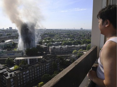 A woman watches as smoke billows from a fire that has engulfed the 24-storey Grenfell Tower in west London, Wednesday June 14, 2017. Fire swept through a high-rise apartment building in west London early Wednesday, killing an unknown number of people with around 50 people being taken to hospital.