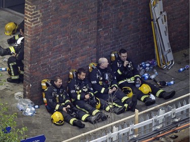 Firefighters rest as they take a break in battling a massive fire that raged in a 27-floor high-rise apartment building in London, Wednesday, June 14, 2017. Fire swept through a high-rise apartment building in west London early Wednesday, killing an unknown number of people and sending more than 50 people to area hospitals.