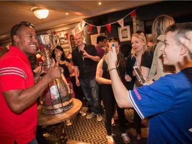 Former CFL quarterback Henry Burris poses for a photo by Allie Laliperte of Midland, Ont., right, with the Grey Cup inside the Maple Leaf Pub in central London on Friday. Jim Ross/CFL