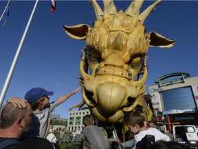 A boy reaches to touch the nose of Long Ma, the horse-dragon, as she sleeps outside City Hall before the evening's La Machine performance in Ottawa on Saturday, July 29, 2017.