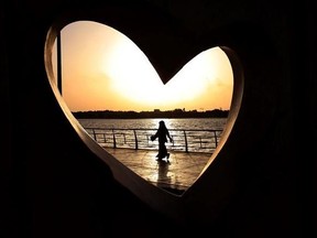 FILE -- In this May 11, 2014 file photo, a Saudi woman seen through a heart-shaped statue walks along an inlet of the Red Sea in Jiddah, Saudi Arabia. A young Saudi woman has sparked a sensation online by posting a video of herself in a miniskirt and crop top walking around in public, with some Saudis calling for her arrest and others rushing to her defense. The video, first shared on Snapchat, shows her walking around an empty historic fort in Ushaiager, a village north of the capital, Riyadh,