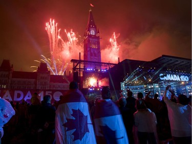 People wearing Canadian flags watch fireworks explode over the Peace Tower during the evening ceremonies of Canada's 150th anniversary of Confederation, in Ottawa on Saturday, July 1, 2017.