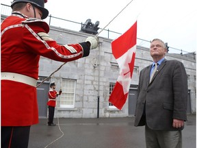Kingston writer and political historian Arthur Milnes watches Cpl. MacGregor Van De Ven, left, and Pvt. Chris Neely of the Fort Henry Guard raise a Canadian flag that once flew over the Peace Tower in Ottawa that Milnes received in Kingston last week.