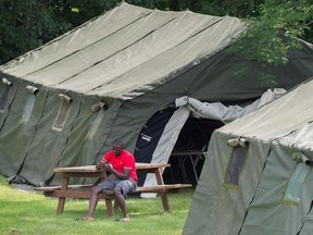 An asylum seeker checks his phone next to a tent at the Canada-United States border in Lacolle, Que. Thursday, August 10, 2017. THE CANADIAN PRESS/Graham Hughes