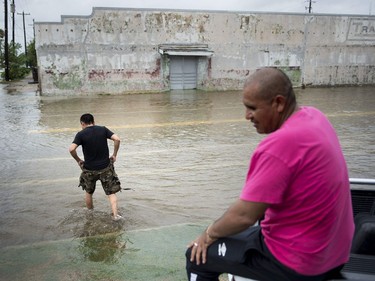 A man wades through water while another sits on a truck as the effects of Hurricane Harvey are seen August 26, 2017 in Galveston, Texas. Hurricane Harvey left a trail of devastation Saturday after the most powerful storm to hit the US mainland in over a decade slammed into Texas, destroying homes, severing power supplies and forcing tens of thousands of residents to flee.