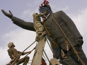 In this file photo taken Wednesday, April 9, 2003, an Iraqi man, bottom right, watches Cpl. Edward Chin of the 3rd Battalion, 4th Marines Regiment, cover the face of a statue of Saddam Hussein with an American flag before toppling the statue in downtown in Baghdad, Iraq.