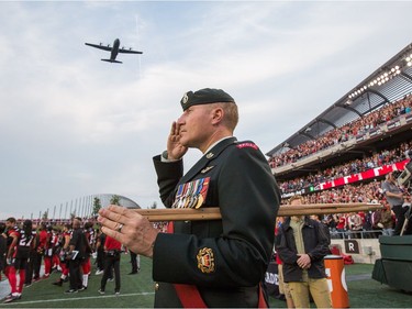 Master Warrant Officer Curtis Hollister salutes as one of two C130 Hercules passes overhead during the opening kickoff ceremonies celebrating the Canadian military as the Ottawa Redblacks take on the Edmonton Eskimos in CFL action at TD Place in Ottawa on Thursday.  Wayne Cuddington/Postmedia