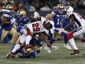 The Redblacks' William Powell (29) gets tackled by the Blue Bombers' Jovan Santos-Knox (45), TJ Heath (23) and Taylor Loffler (16) during the first half of Friday's game. THE CANADIAN PRESS/John Woods