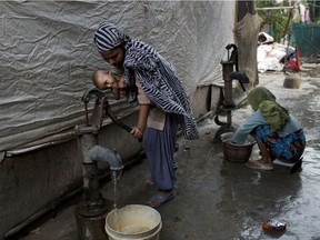 A Rohingya Muslim woman holds a child as she pumps water at a camp for refugees in New Delhi, India, Monday, Sept. 18, 2017.