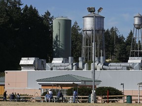 In this Sept. 15, 2017 photo, residents sit in a yard at the Special Commitment Center on McNeil Island, Wash., with the current water tower that serves the facility behind them at left, next to two older and currently unused towers. Scores of sex offenders ordered to live on the secluded island say the water there is making them sick and causing unexplained deaths, and records show the water system has been plagued by problems for more than a decade. (AP Photo/Ted S. Warren)
