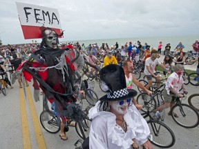 FILE - In this Oct. 22, 2017 file photo provided by the Florida Keys News Bureau, Barry Gibson, left, costumed as the grim reaper, carries a Federal Emergency Management Agency sign while riding in the Fantasy Fest Zombie Bike Ride in Key West, Fla. The flamboyance of Fantasy Fest is a relief for business owners who say they've been trying to weather an economic storm that hit after Hurricane Irma battered the middle stretch of the tourism-dependent island chain last month. (Rob O'Neal/Florida Keys News Bureau via AP, File)