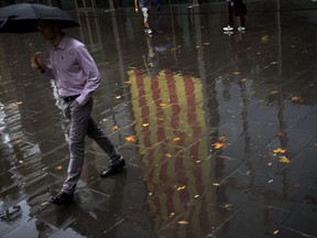 People walk past a Catalan flag reflected on the wet ground in Barcelona, Spain, Thursday, Oct. 19, 2017. Spain's government on Thursday immediately rejected a threat by Catalonia's leader to declare independence unless talks are held, calling a special Cabinet session for the weekend to activate measures to take control of the region's semi-autonomous powers. (AP Photo/Emilio Morenatti)