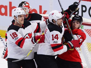 Ottawa Senators centre Jean-Gabriel Pageau, right, gets roughed up in front on the net by the Devils' Adam Henrique (14) and Drew Stafford (16).