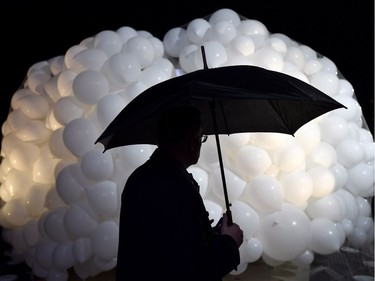 A man shields himself from the rain as he stands in front of balloons obscuring Lord Stanley's Gift Monument before its unveiling on Sparks Street on Saturday. THE CANADIAN PRESS/Justin Tang