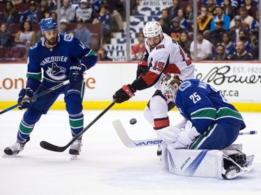 Vancouver Canucks' Erik Gudbranson, left, looks on as teammate Jacob Markstrom, of Sweden, makes the save while Ottawa Senators' Zack Smith (15) reaches for the rebound during first period NHL hockey action in Vancouver on Tuesday, October 10, 2017.