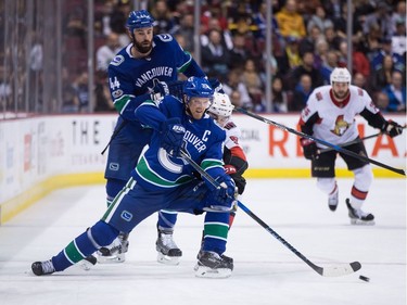 Vancouver Canucks' Henrik Sedin (33), Sweden, is checked by Ottawa Senators' Cody Ceci (5) as Canucks' Erik Gudbranson (44) looks on during first period NHL hockey action in Vancouver on Tuesday, October 10, 2017.