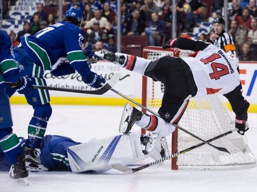 Ottawa Senators' Alex Burrows (14) falls over the net after being stopped by Vancouver Canucks goalie Jacob Markstrom, of Sweden, teammate Ben Hutton (27) looks on during first period NHL hockey action in Vancouver on Tuesday, October 10, 2017.